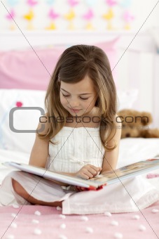 Little girl sitting on bed reading a book