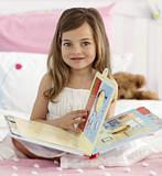Beautiful little girl reading in bed