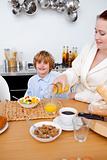 Happy children having breakfast in kitchen with their mother