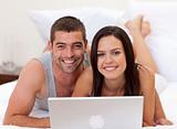 Smiling couple in bed using a laptop