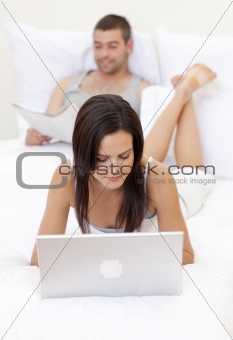 Wife using a laptop and husband reading a newspaper