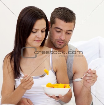 Young couple eating fruit in bed