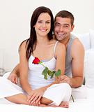 Couple sitting on bed with a rose