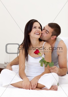 Lovers sitting on bed with a rose