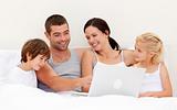 Parents and children using a laptop in bed