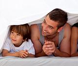Smiling father and son under the bedsheets