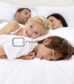 Little girl smiling on bed wile her family sleep