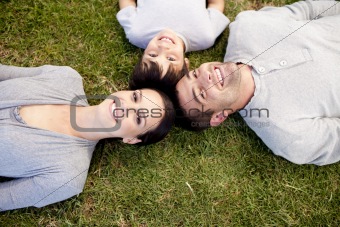 Parents and kid lying on garden with heads together