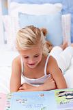 Little girl reading a book in bed