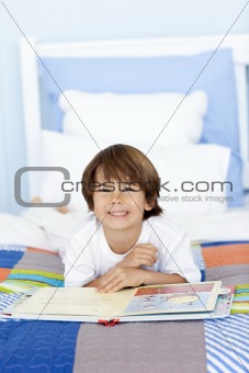 Smiling little boy reading in bed