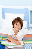 Smiling little boy drawing in bed