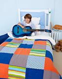 Little boy playing guitar in bedroom