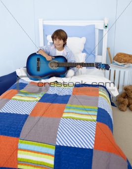 Little boy playing guitar in bedroom