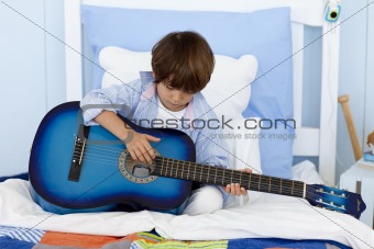 Little boy playing guitar in bed
