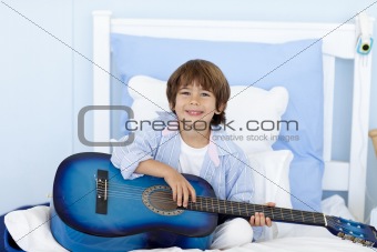 Happy little boy playing guitar in bed