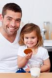 Father and daughter eating biscuits with milk