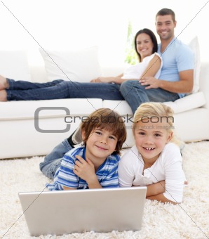 Children playing with a laptop and parents lying on sofa