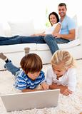 Children using a laptop and couple lying on sofa