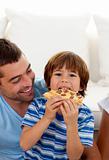 Boy eating pizza in living-room with his father