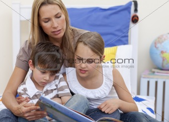 Mother reading a book with her children in bed