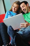 happy couple have fun and work on laptop at home on red sofa