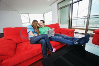 happy couple have fun and work on laptop at home on red sofa