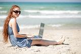 Woman working on a laptop by sitting on the beach