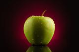 Green apple with drops on red background