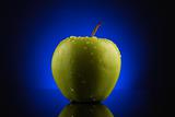 Green apple with drops on blue background