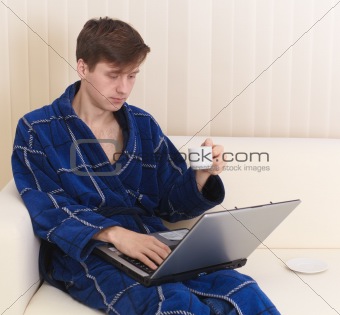 Guy works in Internet on sofa and drinks coffee