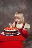 boy with long blond hair watching candles on his birthday cake