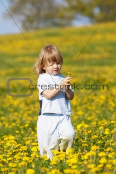 boy with long blond hair holding dandelion standing in a field