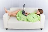 Young beautiful girl lies on sofa in dressing gown with laptop