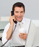 Smiling businessman on phone drinking a coffee in the office