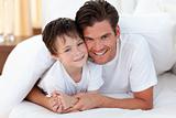 Smiling father and his son lying on bed