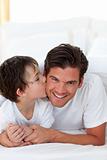 Little boy kissing his father lying on bed