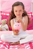 Girl saving money in a piggy bank in her bedroom