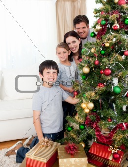Happy family decorating a Christmas tree with boubles and presen