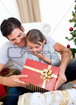 Surprised little daughter opening a Christmas present with her f