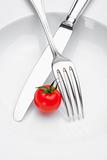 cherry tomato on a plate with fork and knife isolated on white