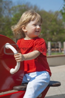 happy boy with long blond hair swinging at the playground