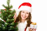 Young smiling Santa Woman near fir tree holds Christmas gift in 