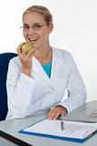 Beautiful female doctor eating an apple while working in her off