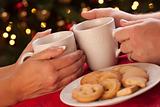 Man and Woman Sharing Hot Chocolate and Cookies in Front of Holiday Lights.