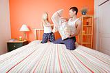 Young Couple Kneeling on Bed Having a Pillow Fight