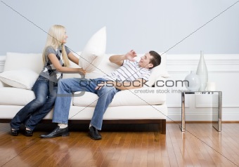 Young Woman Smiling and Hitting Young Man With Pillow