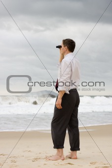 Businessman on a beach searching with binoculars