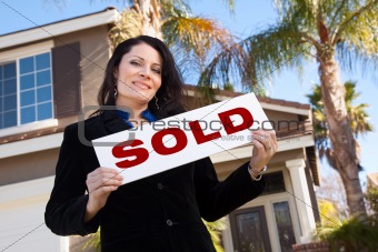 Happy Attractive Hispanic Woman Holding Sold Sign In Front of House.