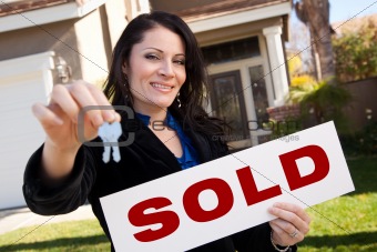 Happy Attractive Hispanic Woman Holding Keys and Sold Sign In Front of House.