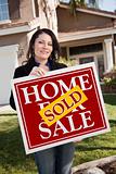 Happy Attractive Hispanic Woman Holding Red Sold Home For Sale Sign In Front of House.